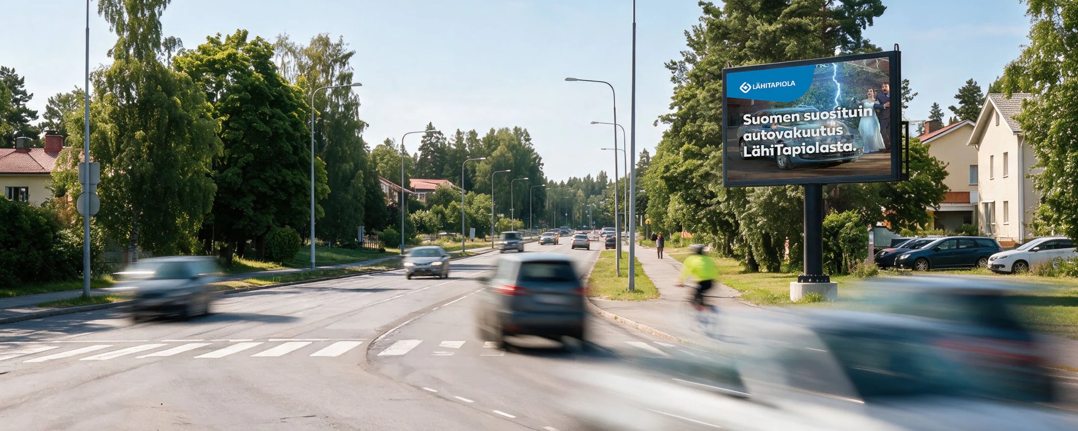 Proscreenin LED-jalustanäyttö vilkkaan tien varrella, ohi ajaa autoja ja pyöräilijä